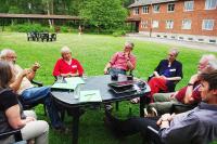 A discussion group are sat around a plastic table outdoors, on a lawn